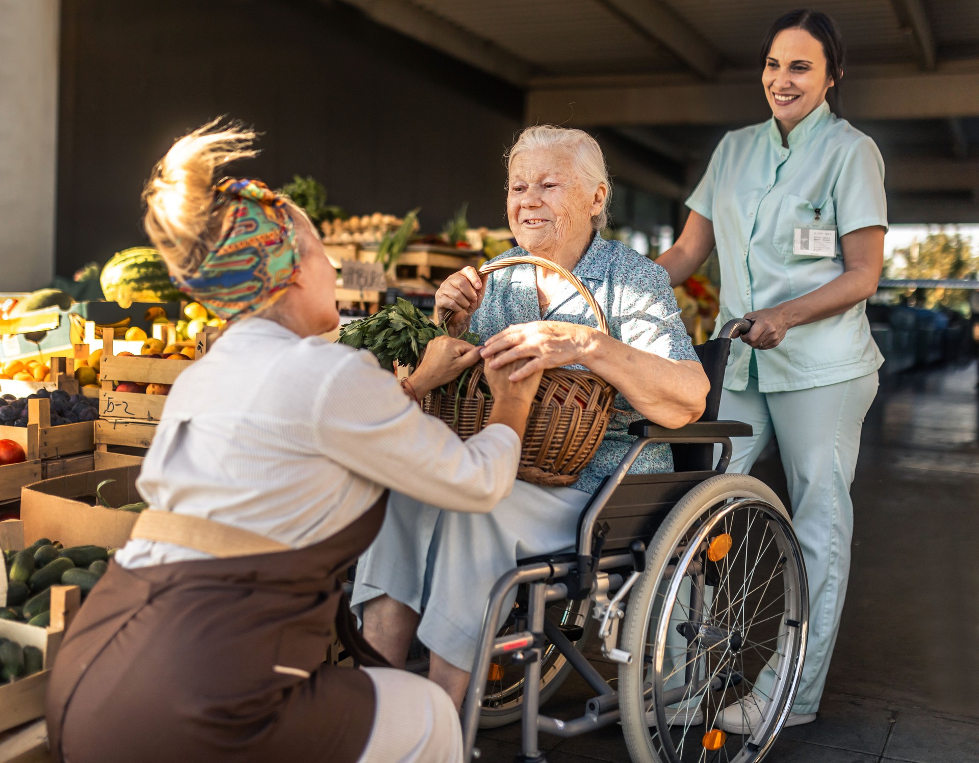 Senior woman in wheelchair shopping for vegetables at farmers market with caregiver